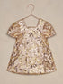 Shiny, sequined gold and pink dress hanging on a hook against a neutral background.