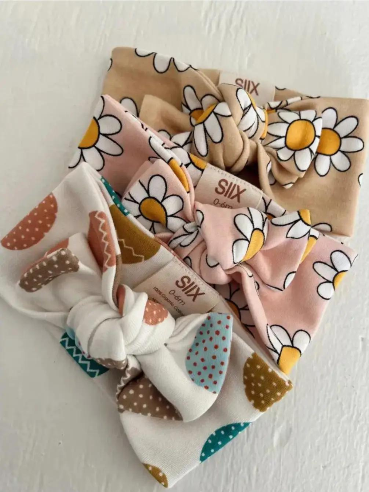 Three colorful fabric headbands with floral and polka dot patterns stacked on a white surface.