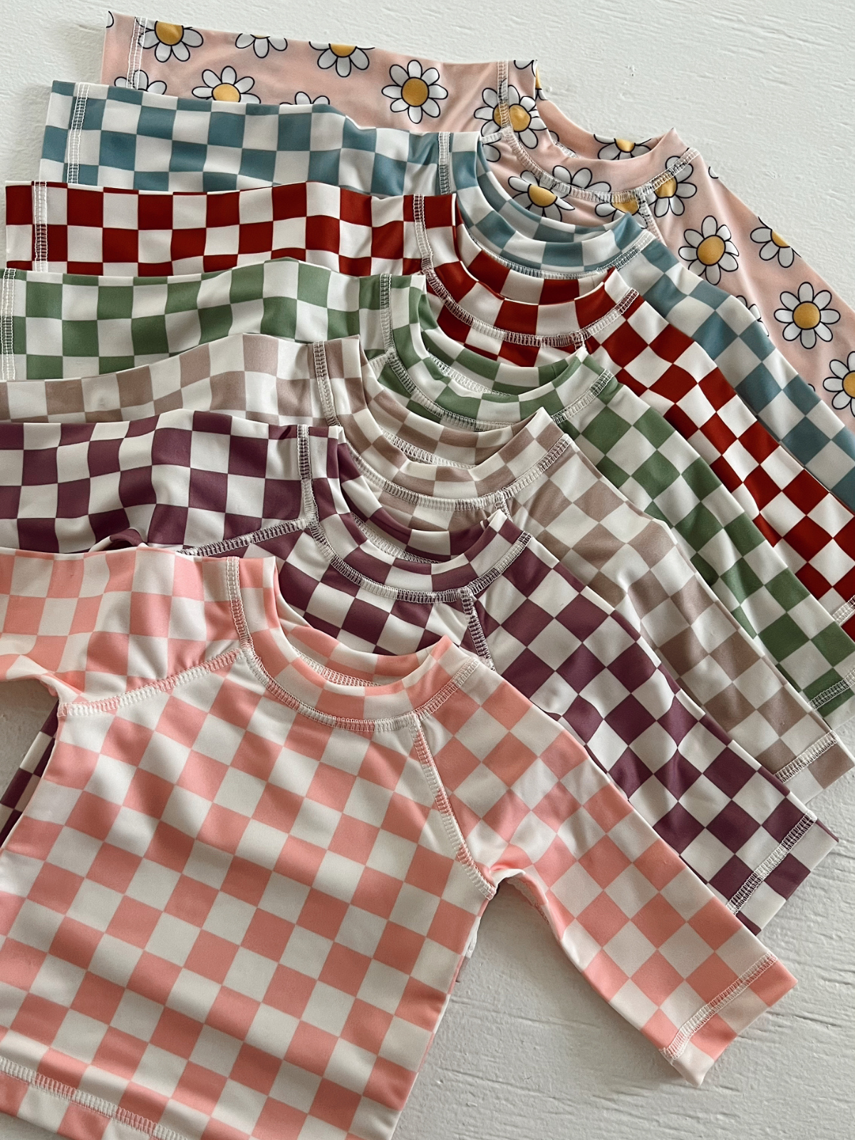 Colorful children's long-sleeve shirts with checkered patterns and floral designs arranged neatly.