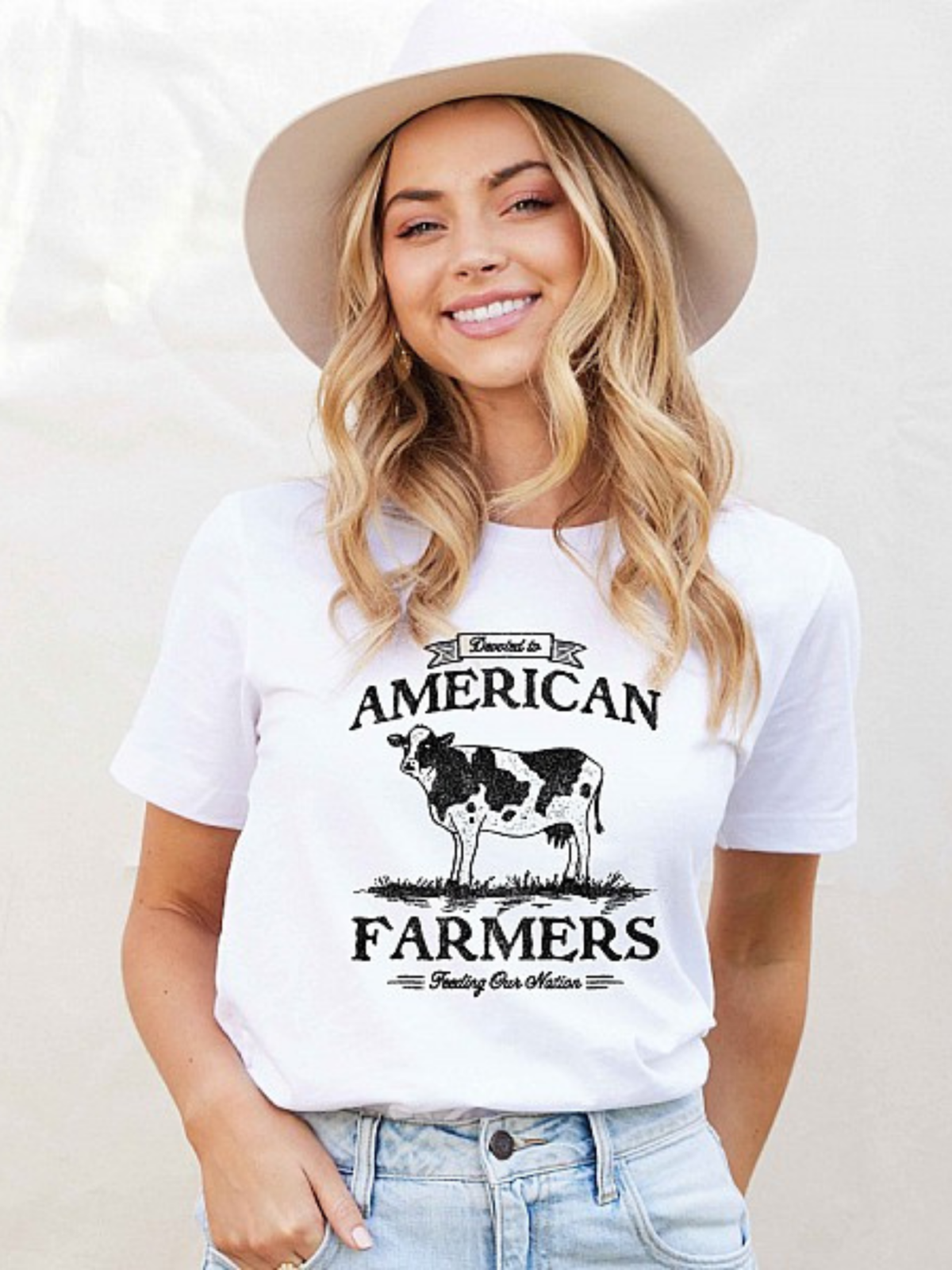 Young woman in a white t-shirt with "American Farmers" and cow graphic, wearing a wide-brimmed hat.