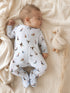 Baby in a duck-patterned onesie sleeping beside a plush toy on a soft blanket.