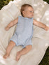 Infant lying on a soft blanket outdoors, wearing a light blue, checkered sleeveless romper.