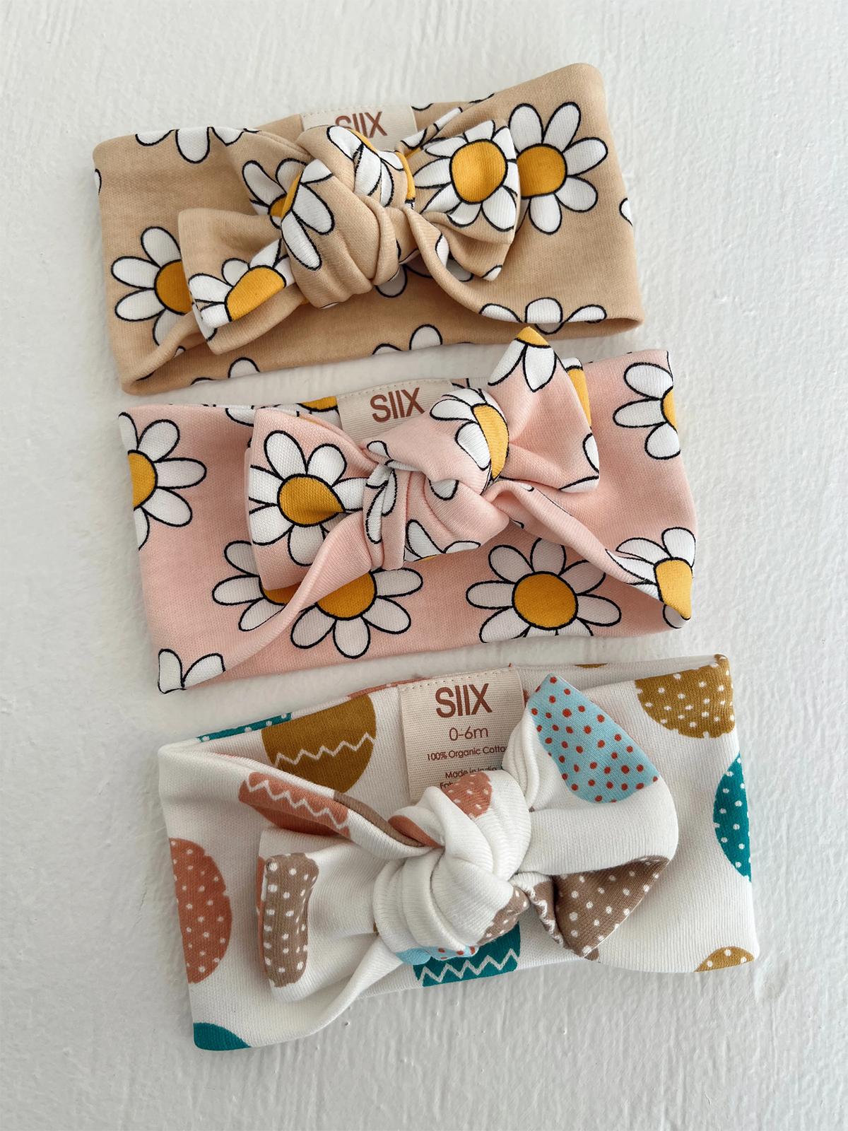 Three baby headbands in floral and polka dot patterns, various colors, displayed on a textured white background.