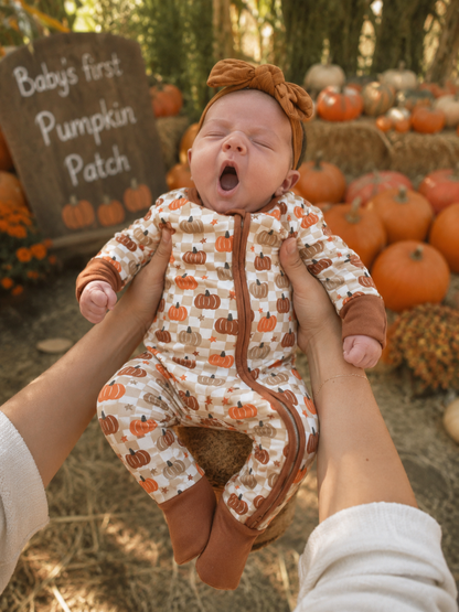 Baby in pumpkin-themed outfit yawning, held up in front of a "Baby's first Pumpkin Patch" sign and pumpkins.