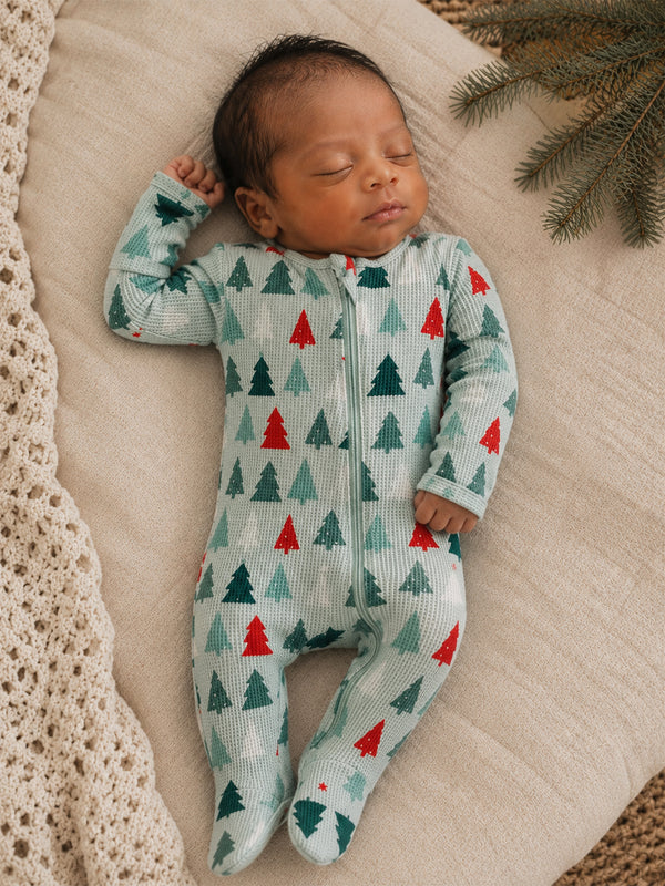 Infant sleeping on a soft blanket, wearing a festive green onesie with red and green Christmas trees.