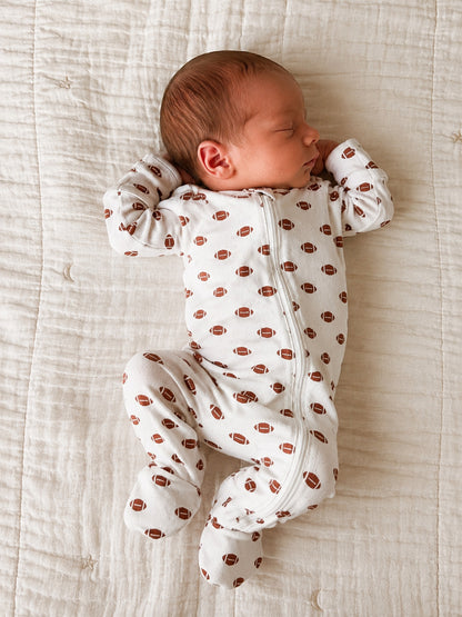 Newborn baby sleeping peacefully in a football-patterned onesie on a soft quilted blanket.