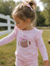 Little girl in a pink long-sleeve shirt with a football and bow design, playing outdoors.