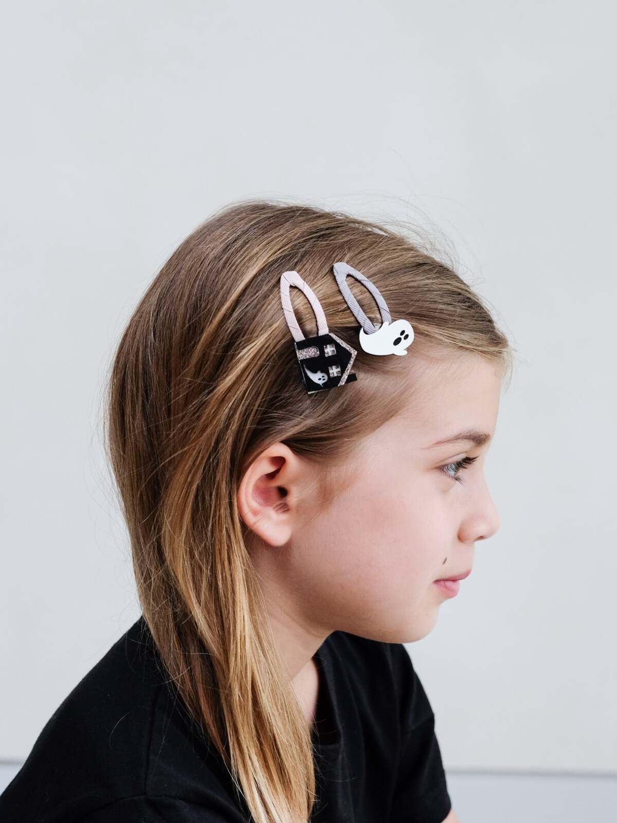 Girl with long hair wearing cute hair clips featuring a bunny and ghost design, against a neutral background.