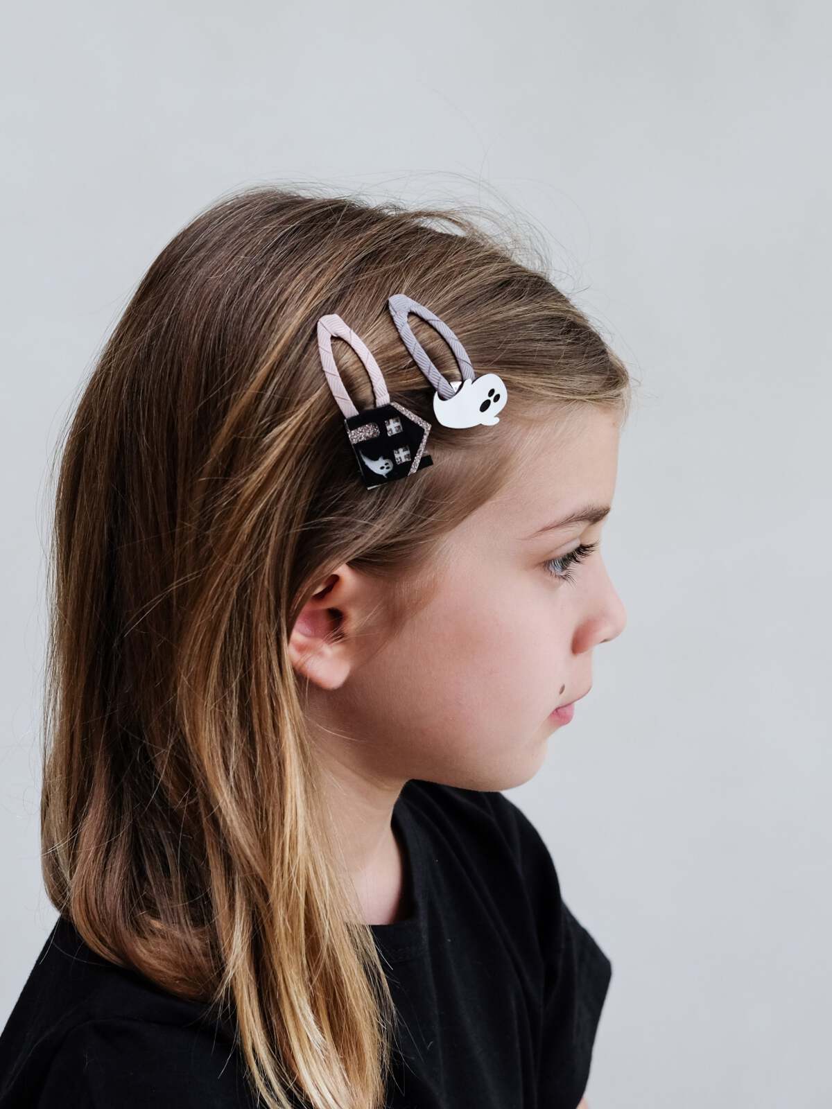 Girl with long hair wearing bunny-shaped hair clips, side profile against a light gray background.
