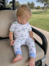 Toddler in golf-themed pajamas sitting on a golf cart seat, with a green landscape in the background.