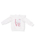 White sweatshirt with ruffle sleeves featuring the word "LOVE" and a decorative polka dot design.