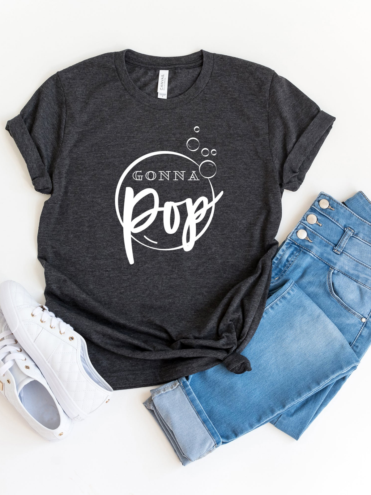Gray t-shirt with "Gonna Pop" design, paired with blue jeans and white sneakers, laid flat on a white background.