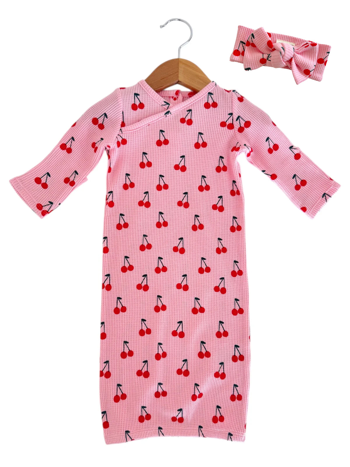 Pink baby dress with cherry pattern and matching headband, hanging on a wooden hanger.