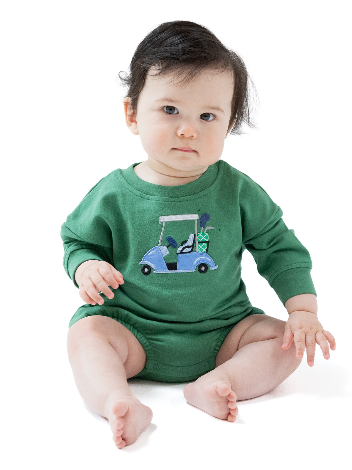 Baby in a green outfit with an embroidered golf cart design, sitting with a thoughtful expression.