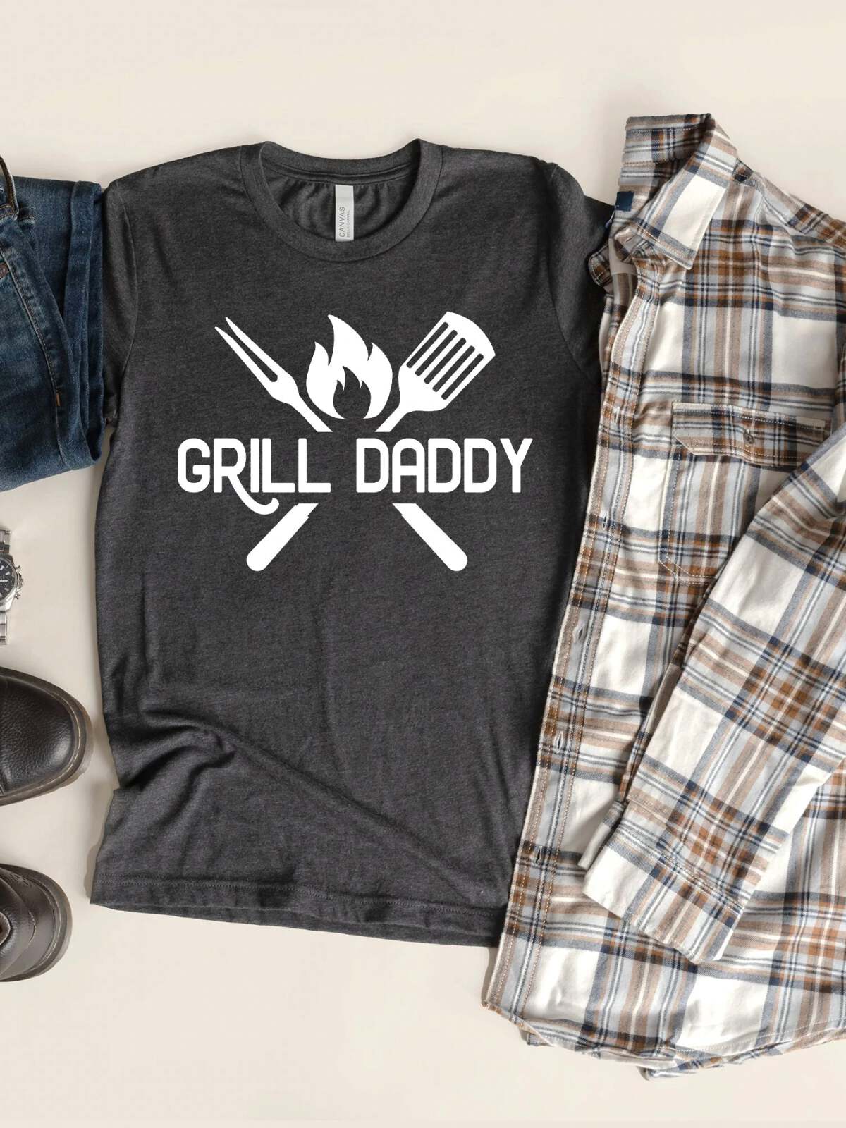 Gray t-shirt with "GRILL DADDY" graphic and grilling tools, paired with jeans and a plaid shirt.