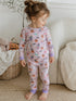 Toddler in Halloween-themed pajamas with pumpkins and ghosts, standing beside a cozy basket and plush toys.