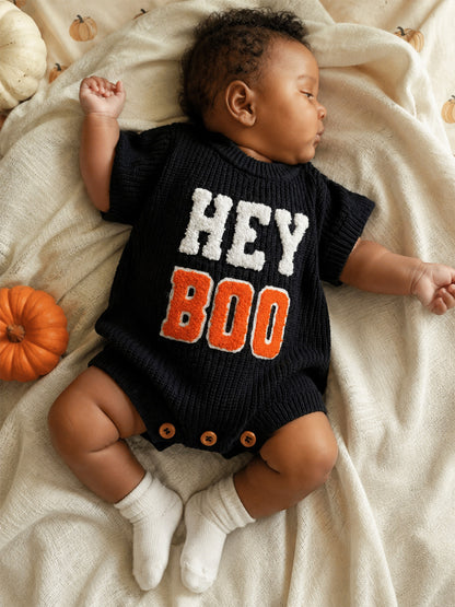 Baby wearing a navy "HEY BOO" outfit, sleeping on a cozy blanket with pumpkins nearby.