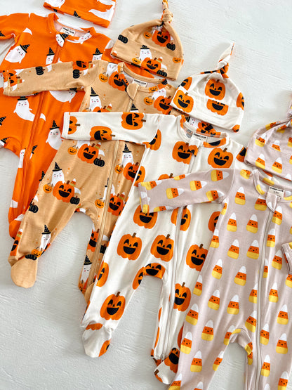 Colorful baby Halloween pajamas and hats with pumpkin, ghost, and candy corn patterns displayed on a light background.