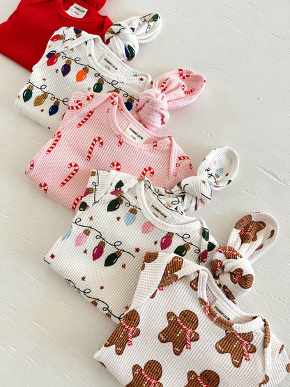 Colorful baby clothes in holiday patterns, including candy canes, lights, and gingerbread, laid out on a white surface.