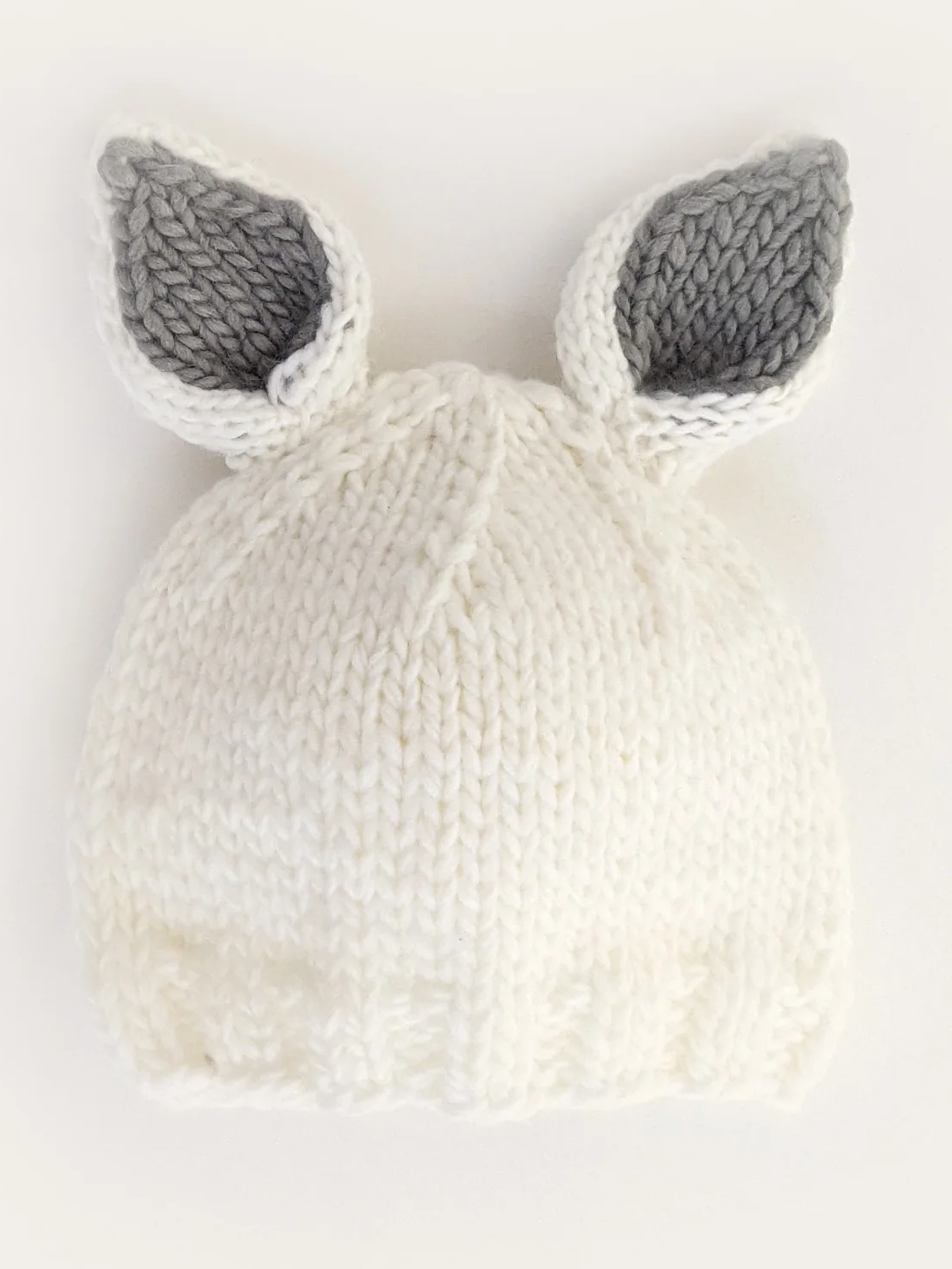 White knitted hat with gray inner ears, designed for children, featuring a textured pattern.