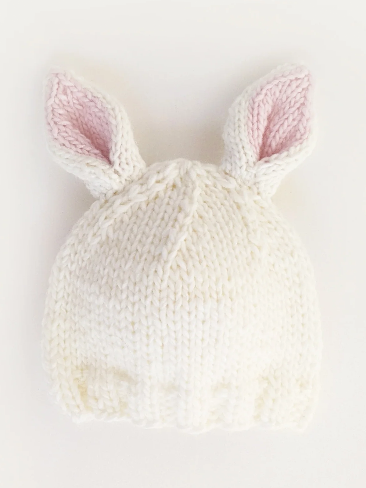 White knitted hat with pink inner bunny ears, resting on a white background.