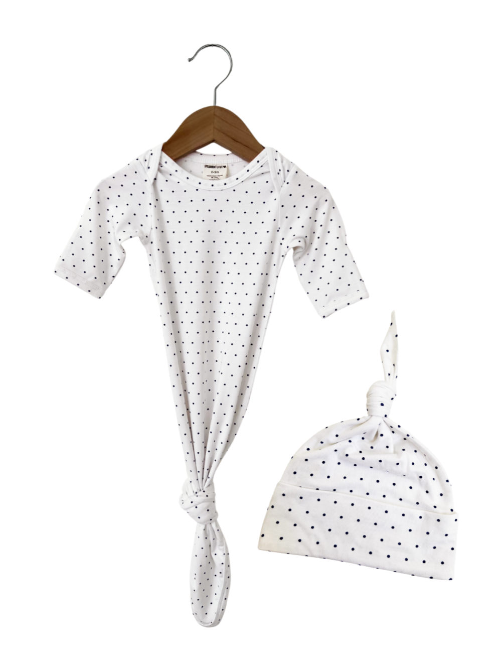 White newborn outfit with navy polka dots, featuring a knotted gown and matching hat on a wooden hanger.
