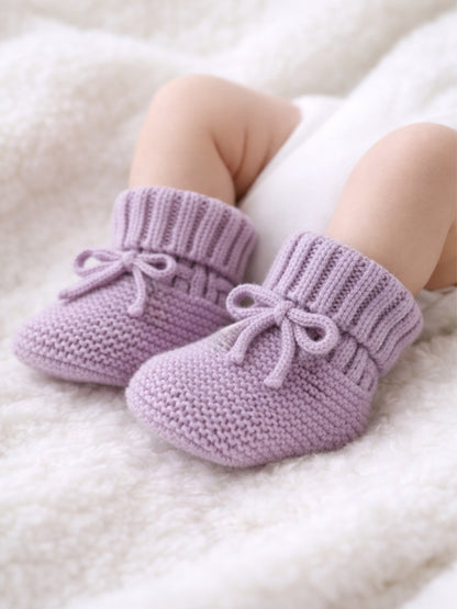 Soft lavender knitted baby booties on a fluffy white blanket, perfect for keeping little feet warm.