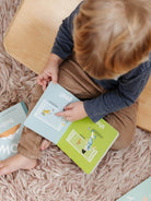 Child reading an illustrated soccer book while sitting on a soft rug, barefoot, with books around.