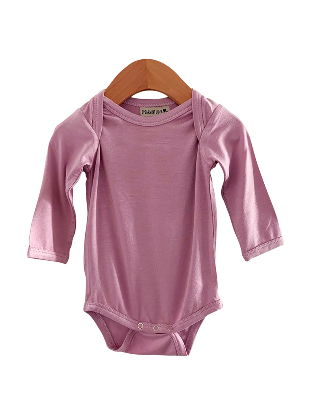 Light pink long-sleeve baby onesie hanging on a wooden hanger against a white background.