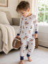 Young boy in playful pajamas with teddy bears, holding a decorative football in a cozy living room setting.