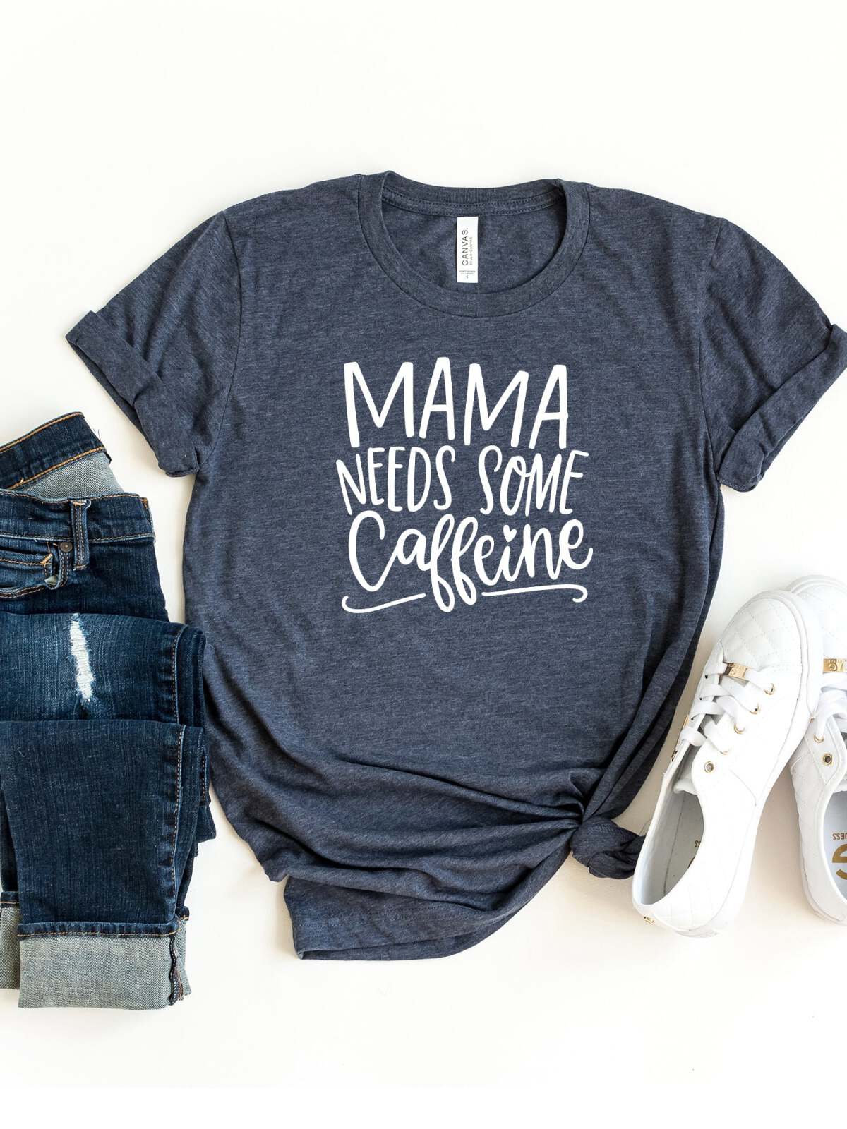 Navy t-shirt with white text that reads "Mama Needs Some Caffeine," styled with jeans and sneakers.