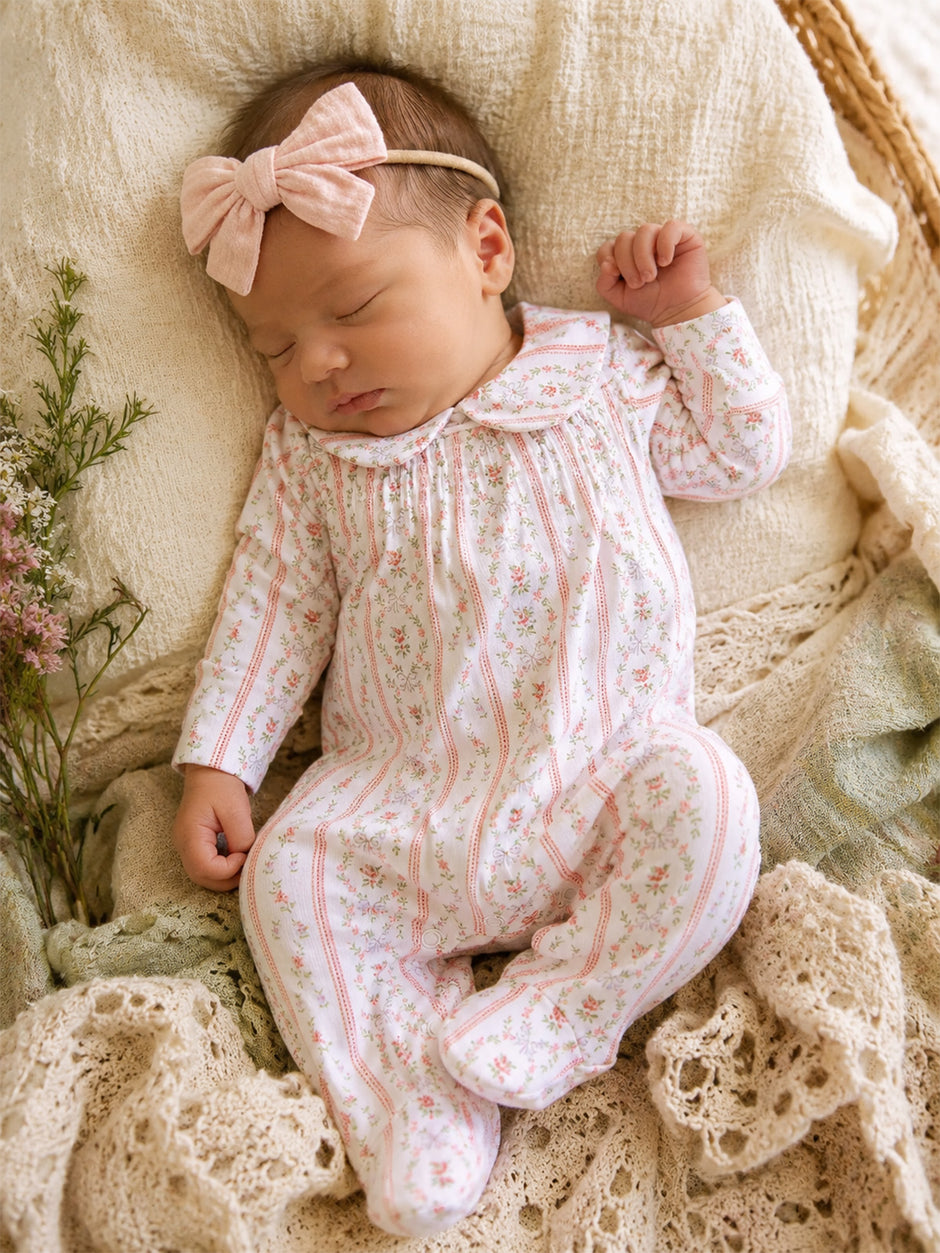 Sleeping baby girl in floral outfit and bow headband, nestled on a soft, textured blanket.