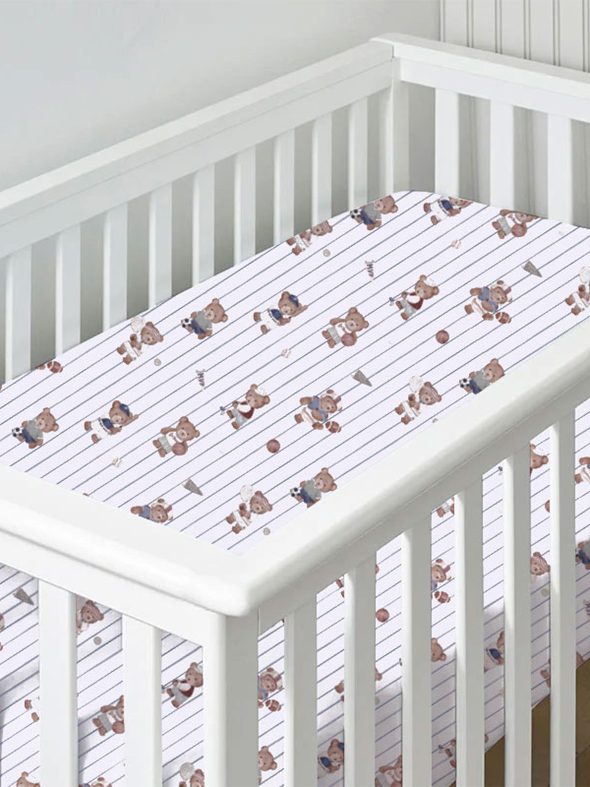 Crib with a sports-themed fitted sheet featuring playful bear illustrations and striped design.