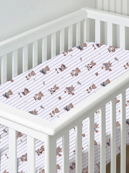 Crib with a sports-themed fitted sheet featuring playful bear illustrations and striped design.