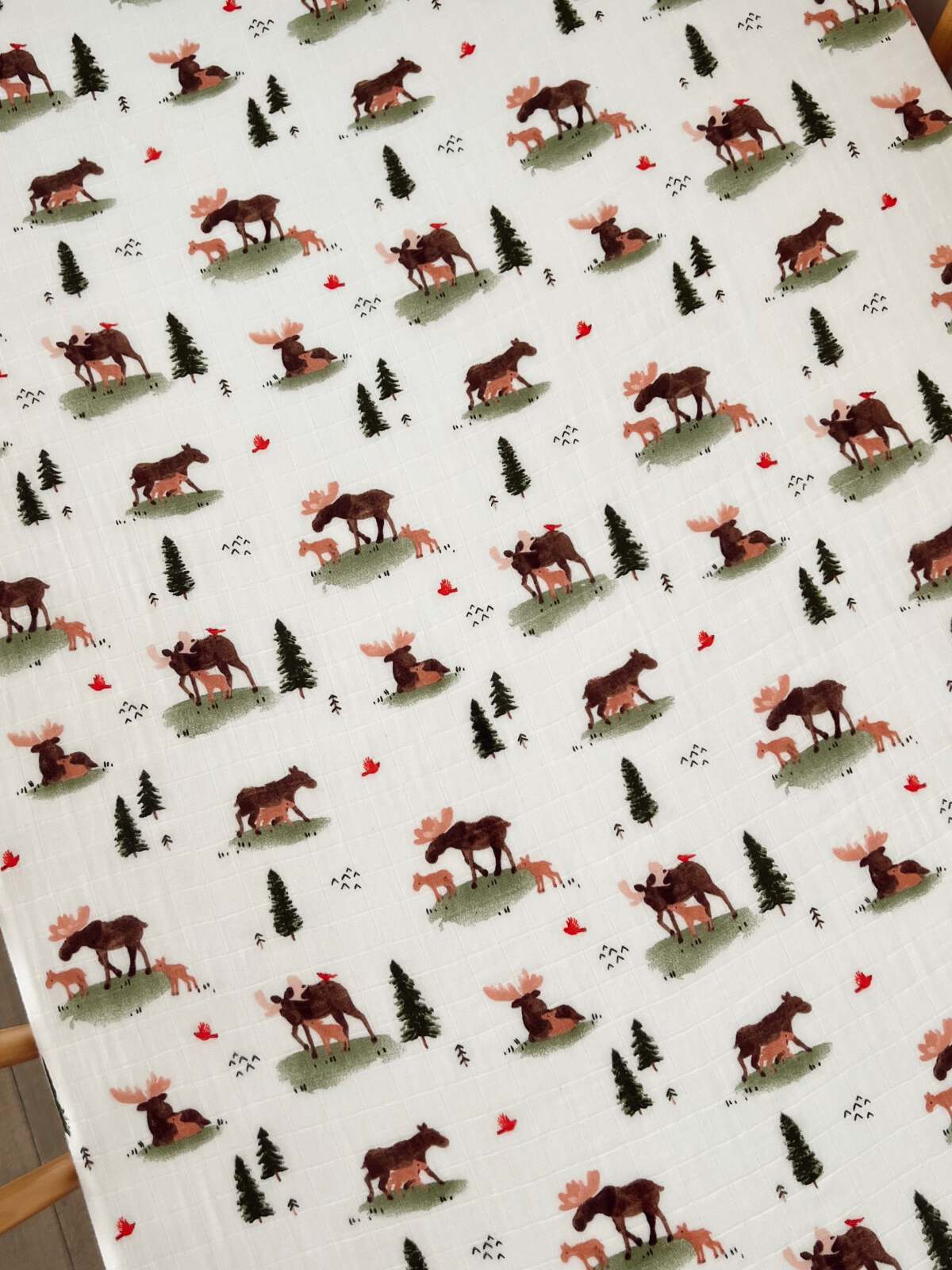 Fabric featuring moose, foxes, trees, and red birds in a playful, nature-inspired pattern.