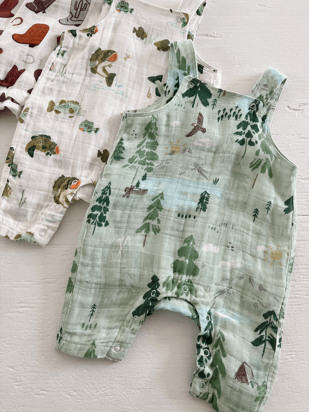 Three colorful baby rompers with nature-themed prints: fish, trees, and camping scenes, on a light background.
