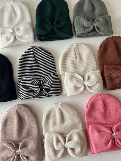 A collection of colorful beanies with bows, arranged neatly on a light background.