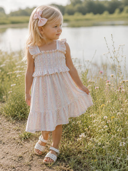 Girl in a pastel dress with a bow, walking through flowers by a calm pond.