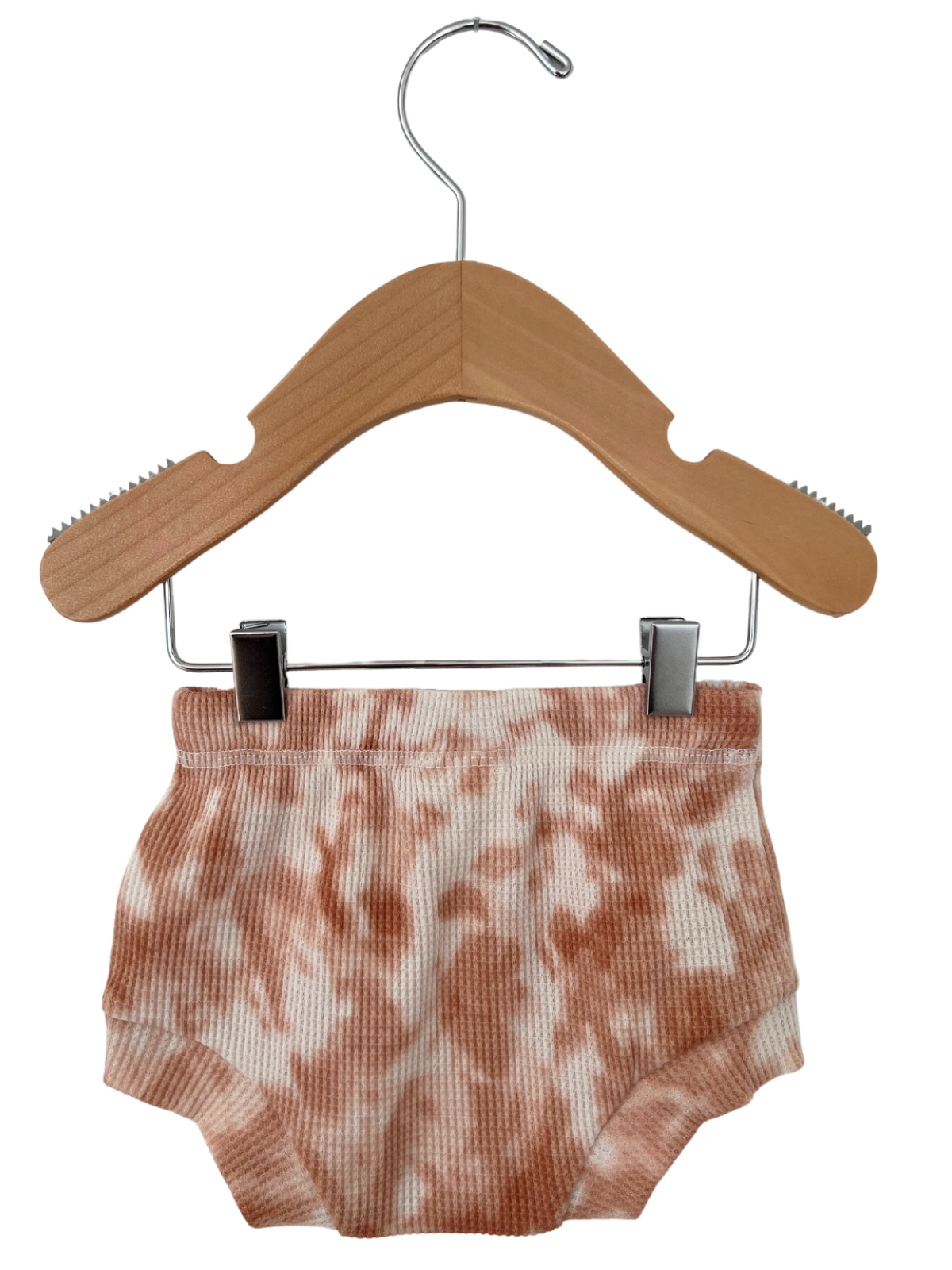 Light pink tie-dye children's shorts on a wooden hanger against a white background.