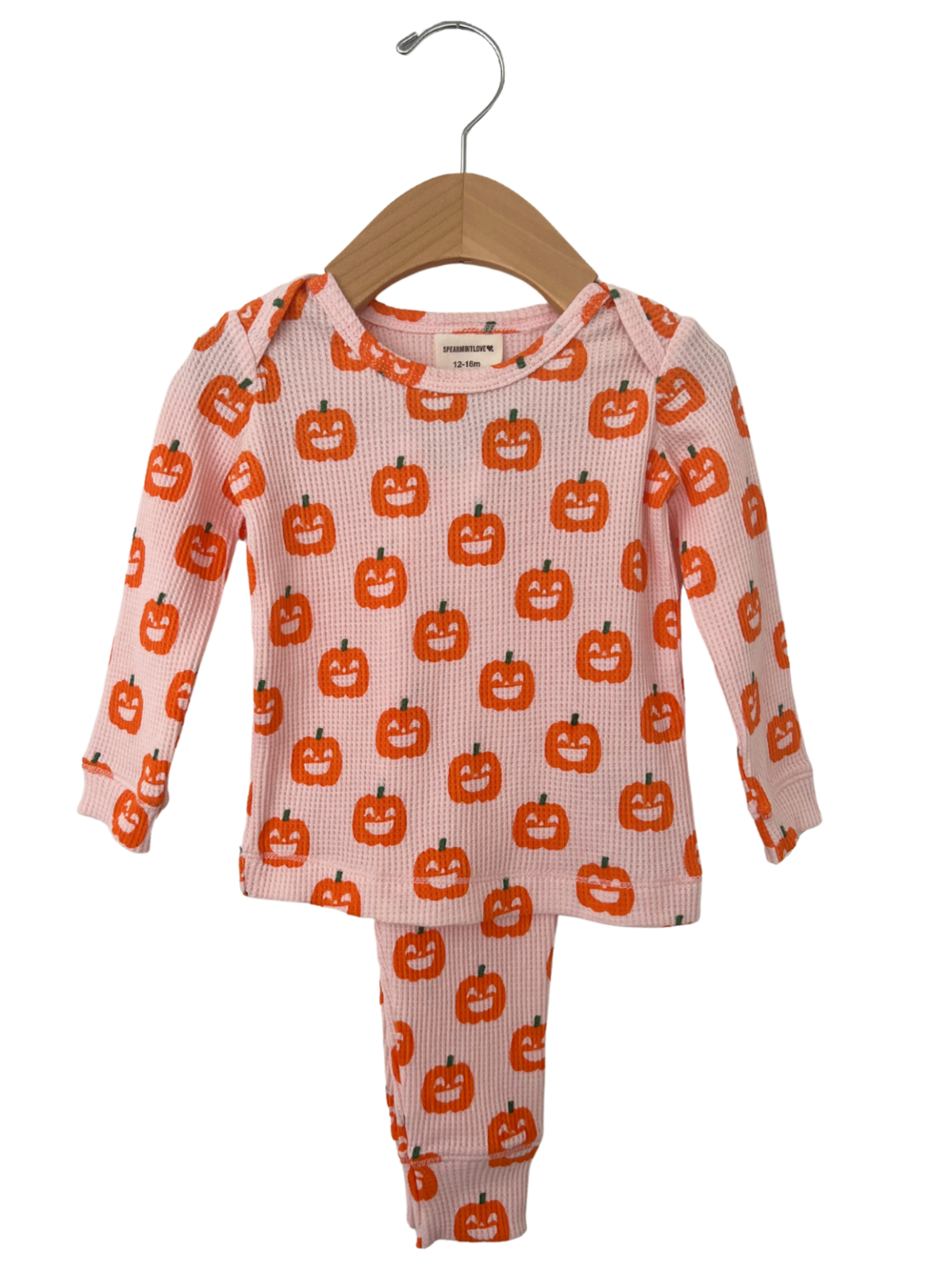 Pink toddler pajama set with orange pumpkin print, hanging on a wooden hanger.