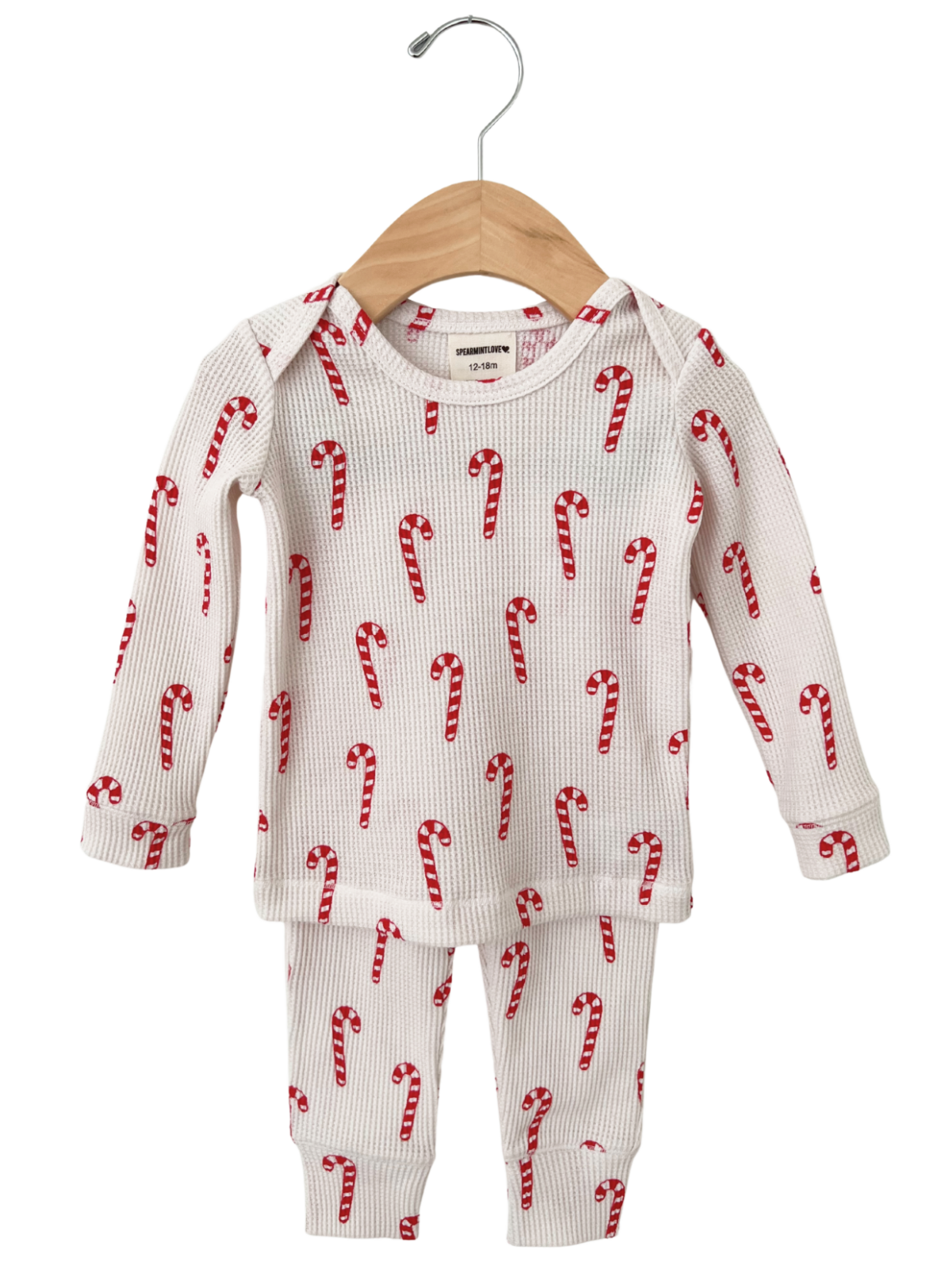 White children's pajama set with red candy cane print, hanging on a wooden hanger. Size 12-18 months.