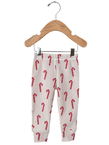 Kid's ribbed leggings with red and white candy cane pattern, displayed on a wooden hanger.