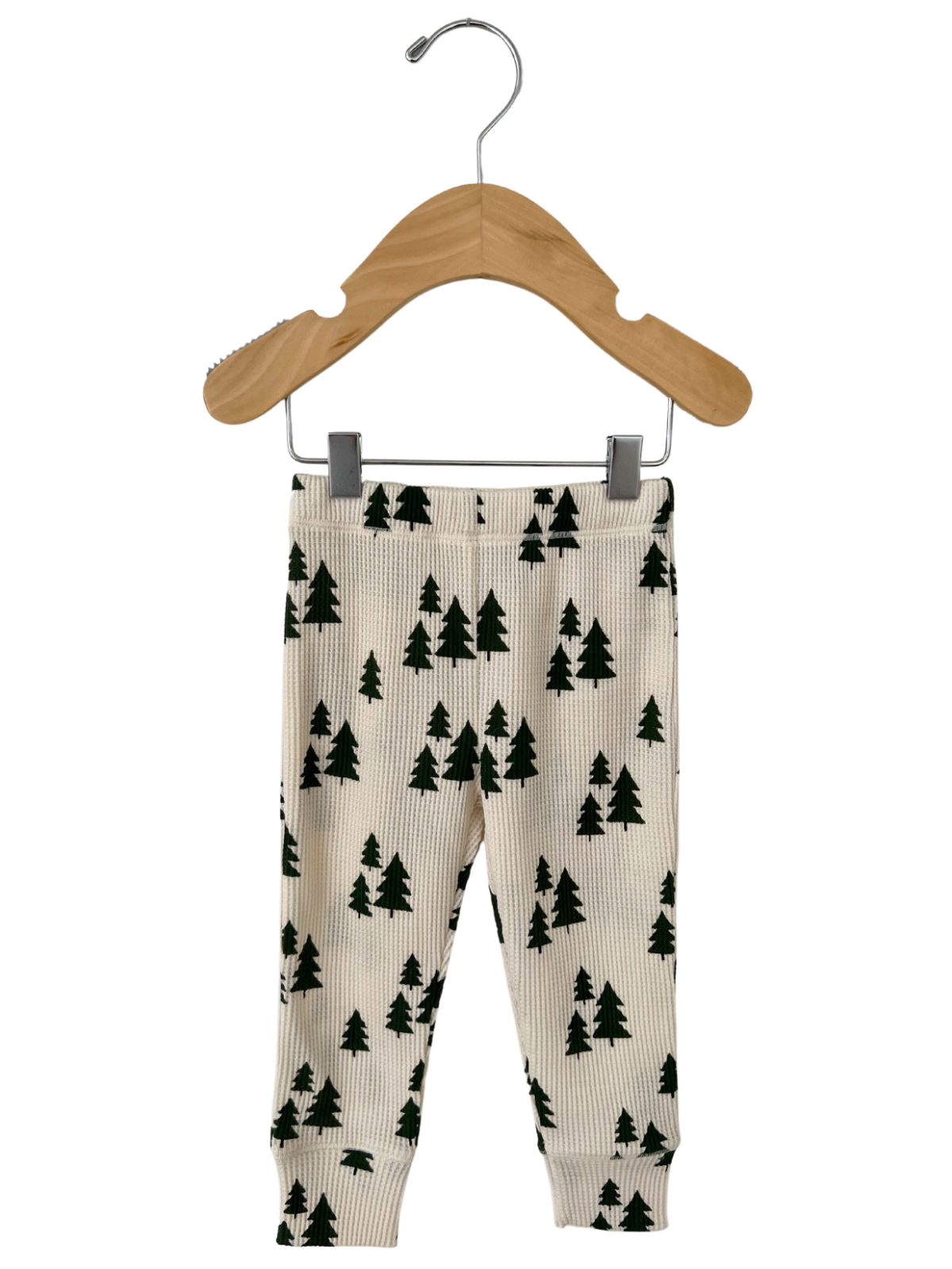 Cream colored leggings with green tree patterns hanging on a wooden hanger.