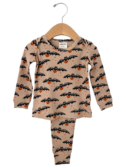 Tan bat and pumpkin patterned children's pajama set hanging on a wooden hanger.