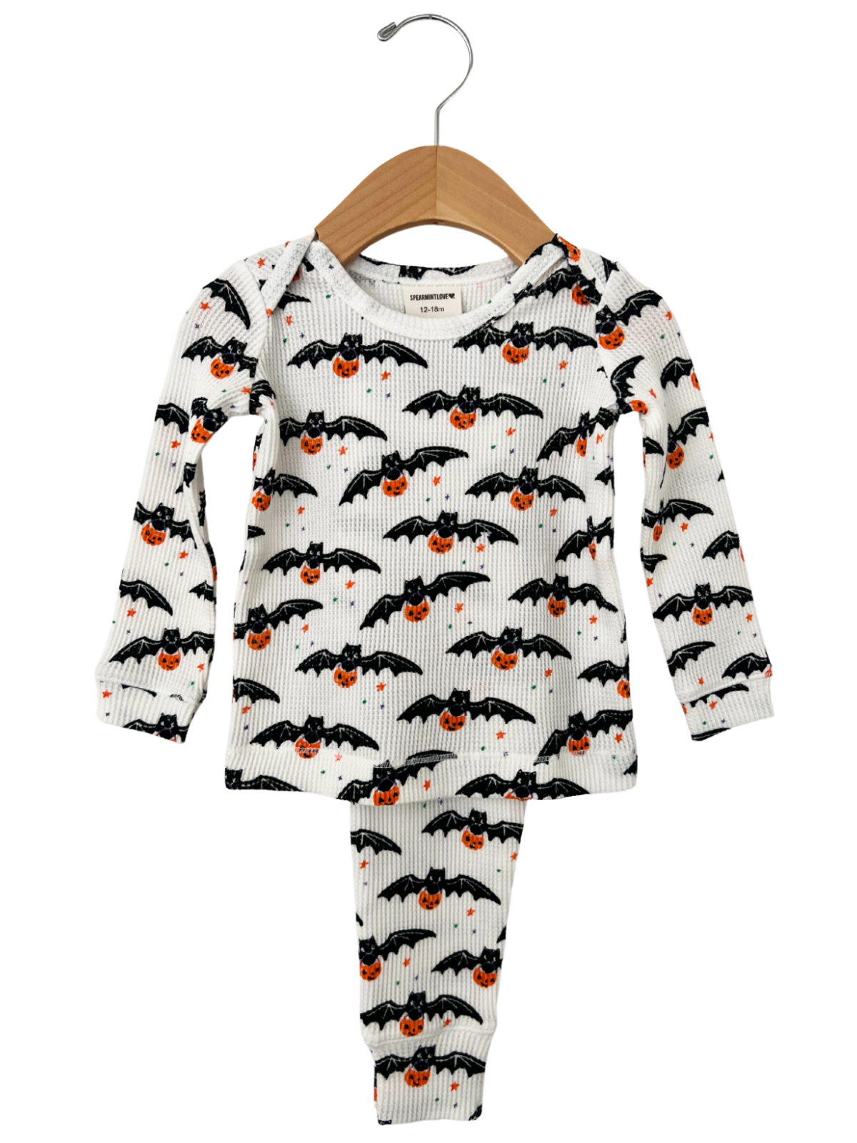 Halloween-themed children's pajamas with bats and pumpkins on a white background, hanging on a wooden hanger.