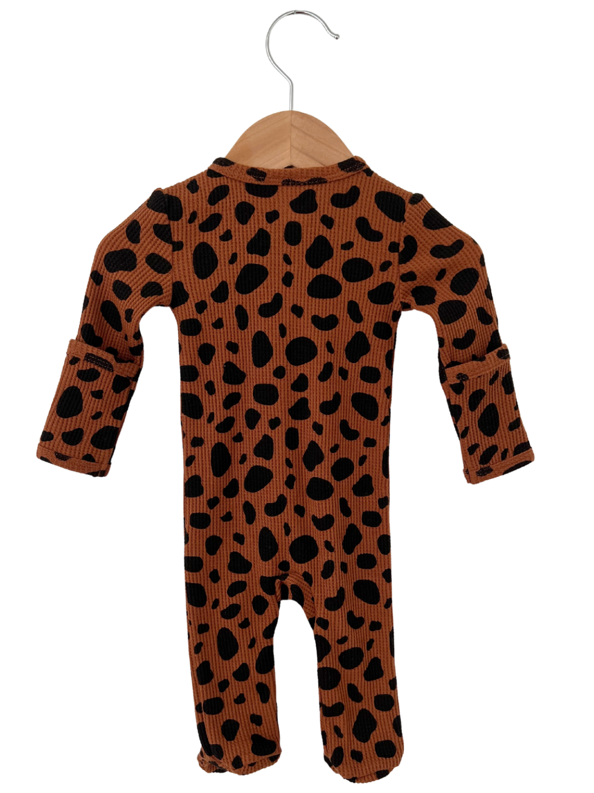 Brown and black polka dot baby onesie hanging from a wooden hanger.