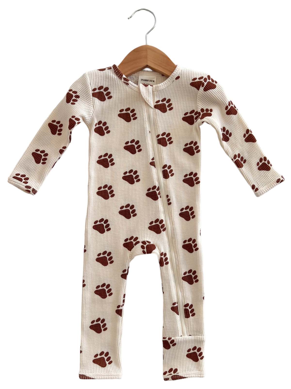 Children's one-piece pajama with brown paw print pattern, hung on a wooden hanger against a neutral background.