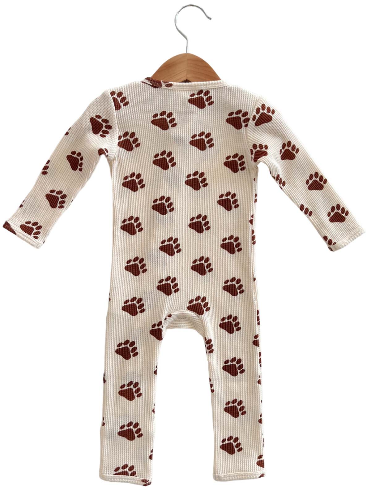 Cream baby onesie with brown paw print pattern, displayed on a wooden hanger. Back view, long sleeves.
