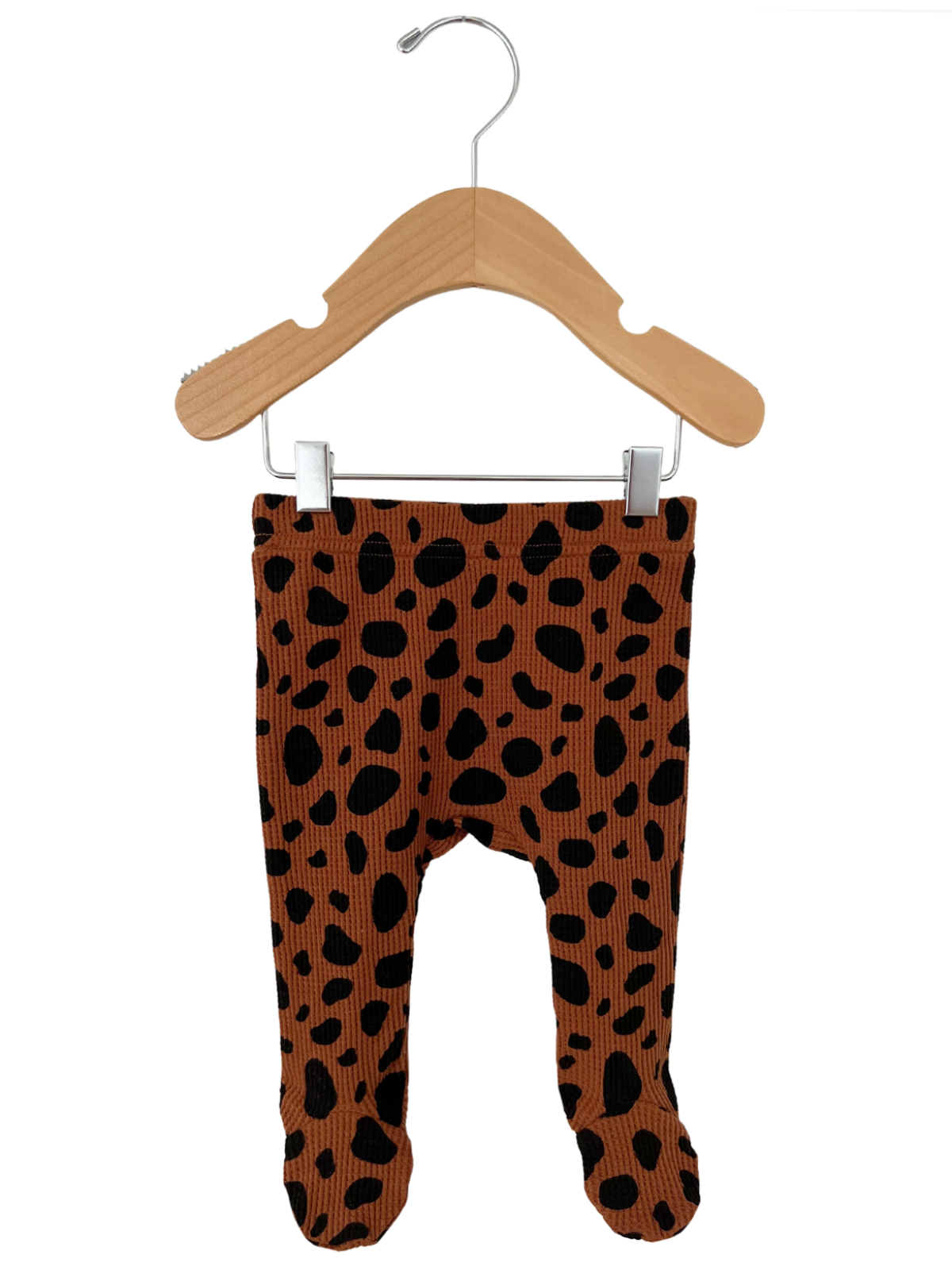 Brown and black spotted toddler leggings hanging on a wood hanger against a white background.