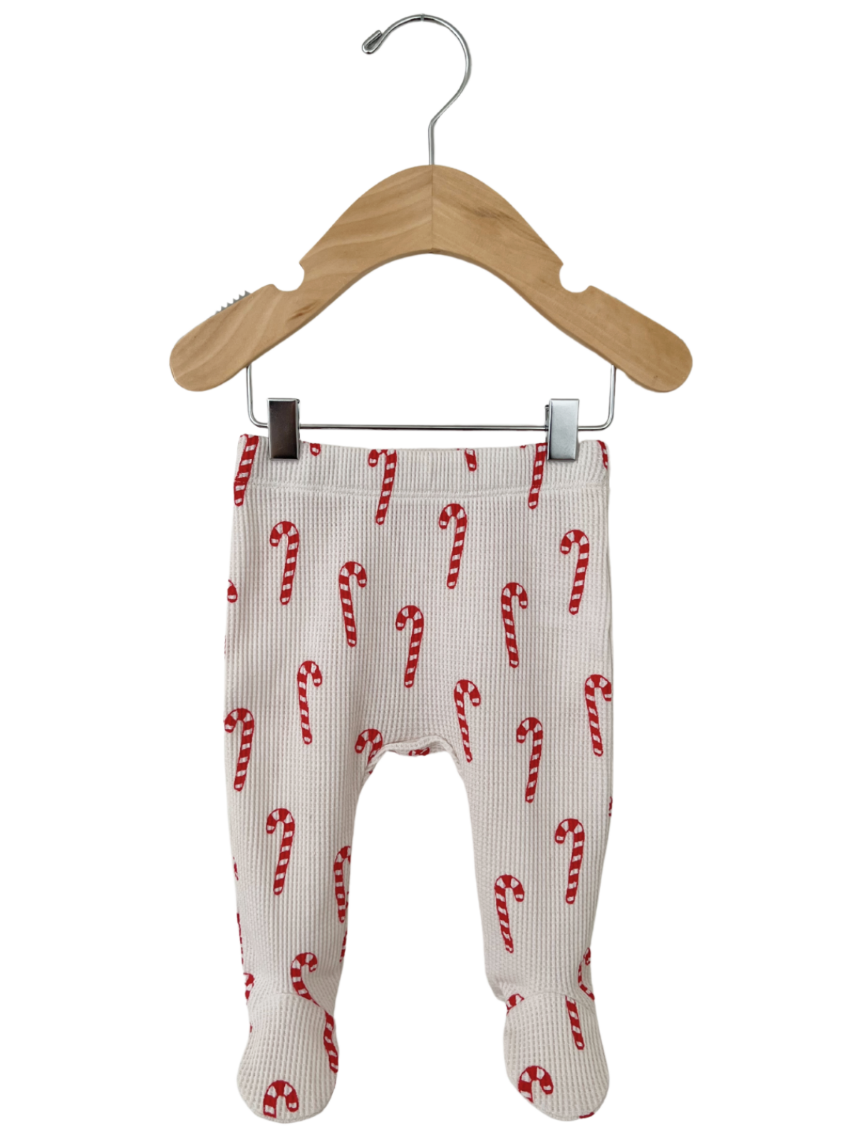 Red and white candy cane patterned baby leggings hanging on a wooden hanger.